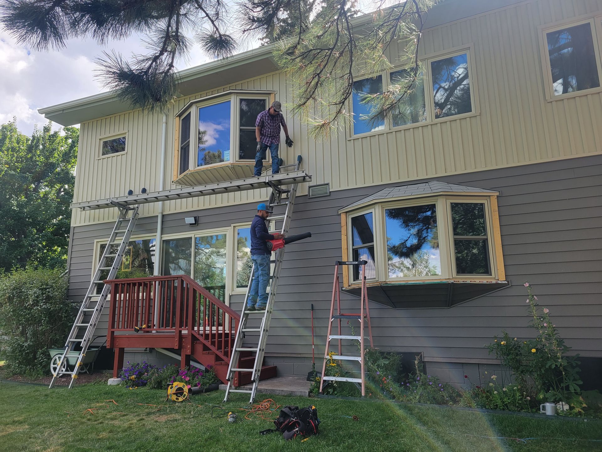 Two people on ladders cleaning and working on a two-story house with bay windows.