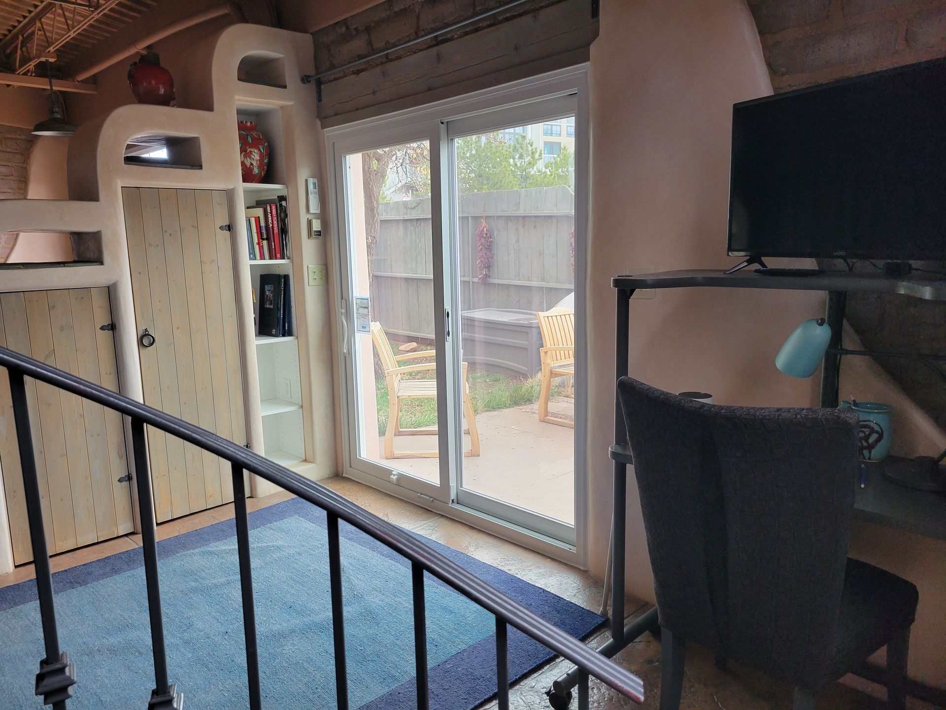 Interior with sliding glass door to patio; built-in shelves, blue rug, black desk with chair and TV.