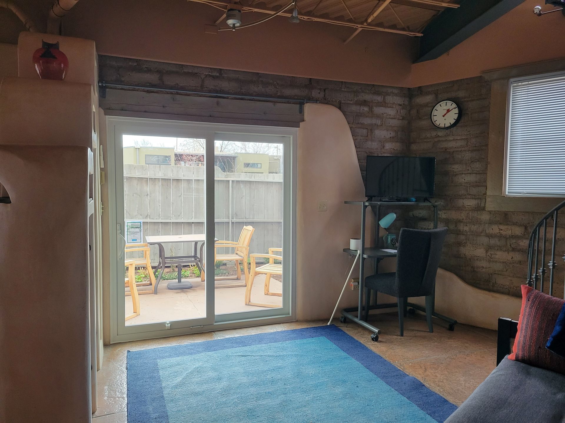Room with sliding door to patio, desk, blue rug, brick wall, and clock.