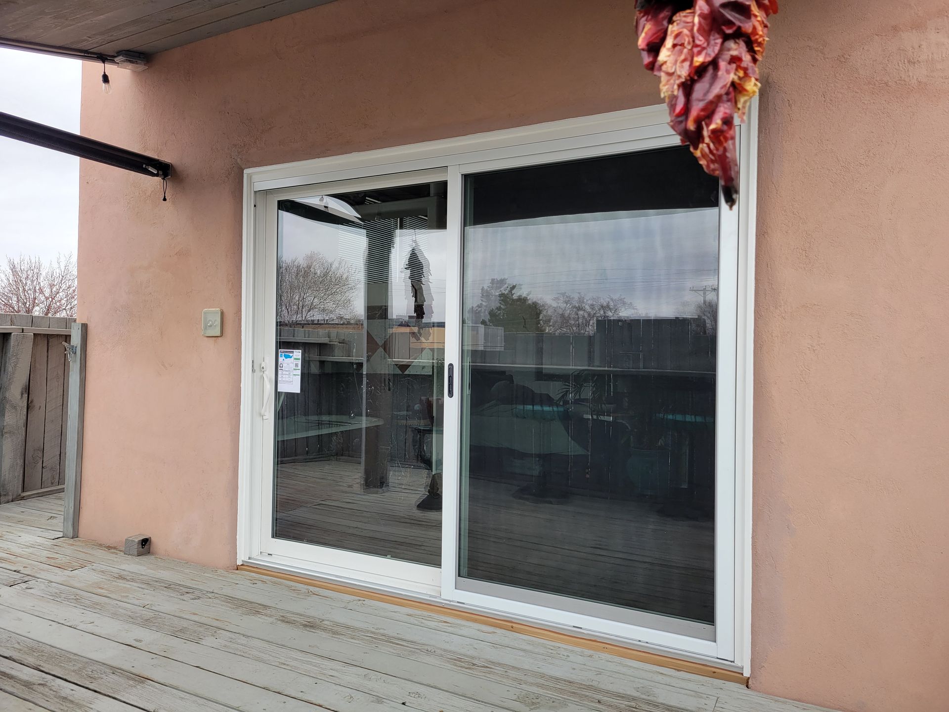 Sliding glass door on a stucco building with a wooden deck, dark screen, and a string of chili peppers.