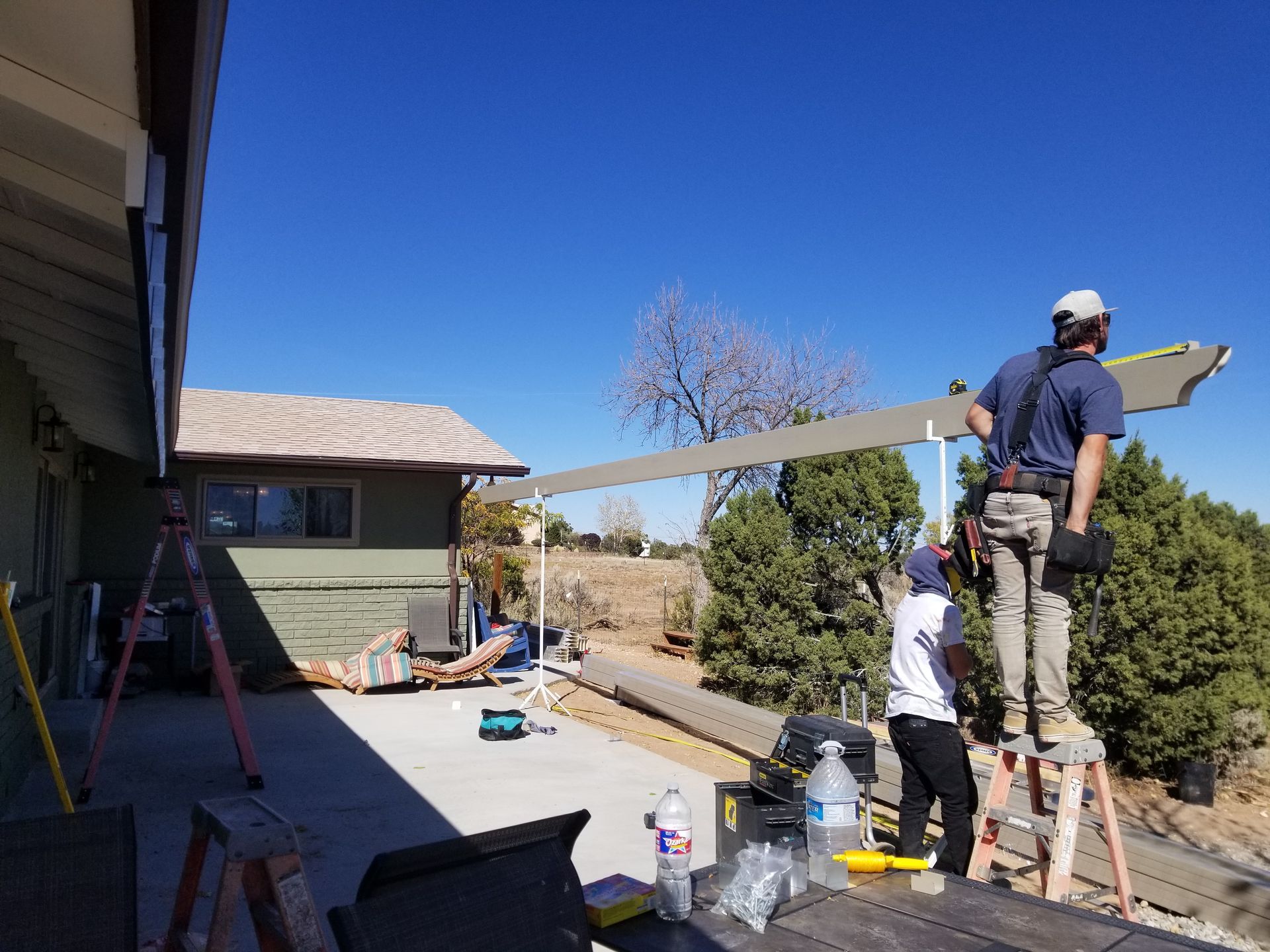 Two workers install a roof extension on a sunny day.