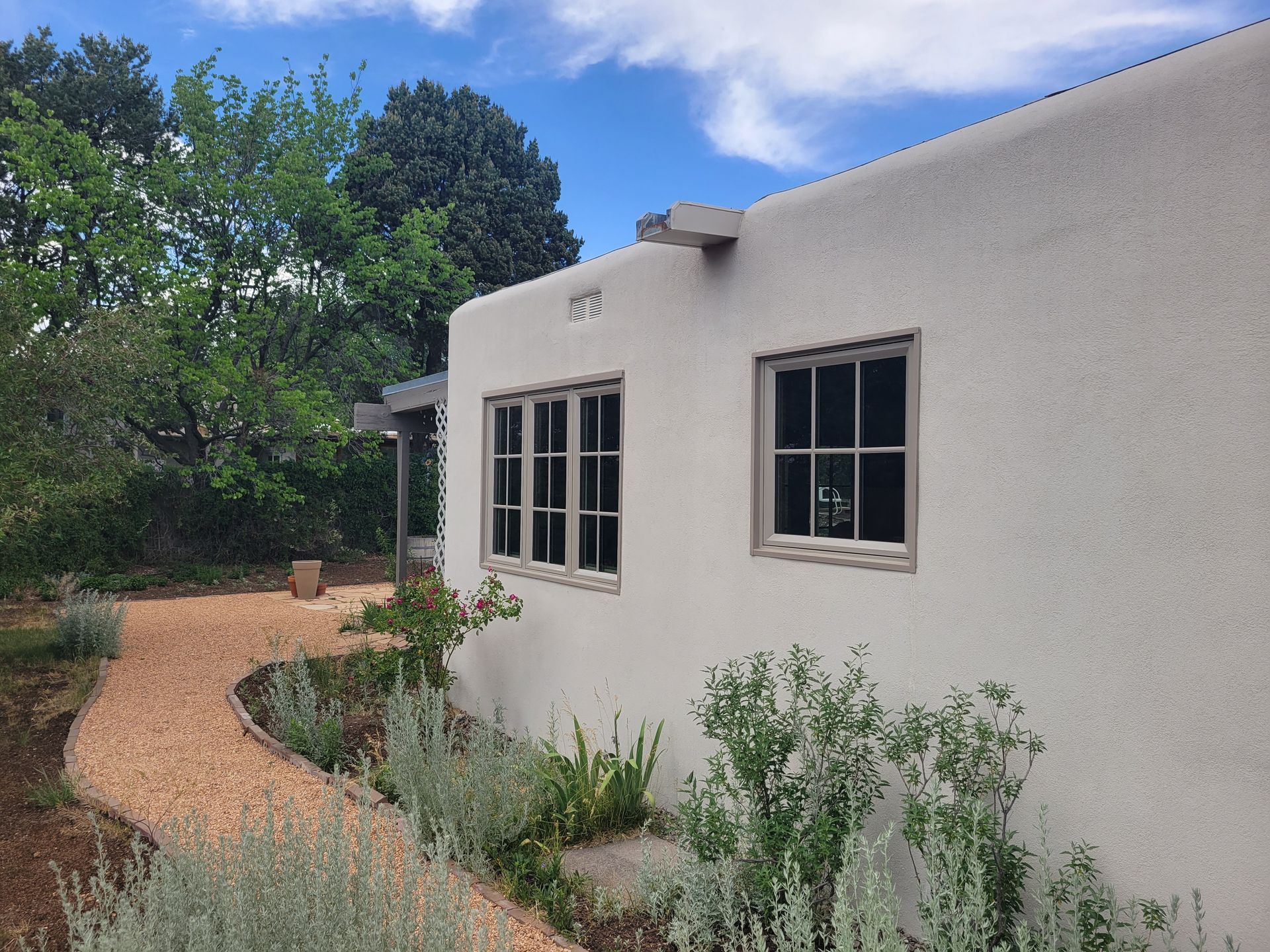 Beige stucco building with windows, gravel path, and plants under a blue sky.