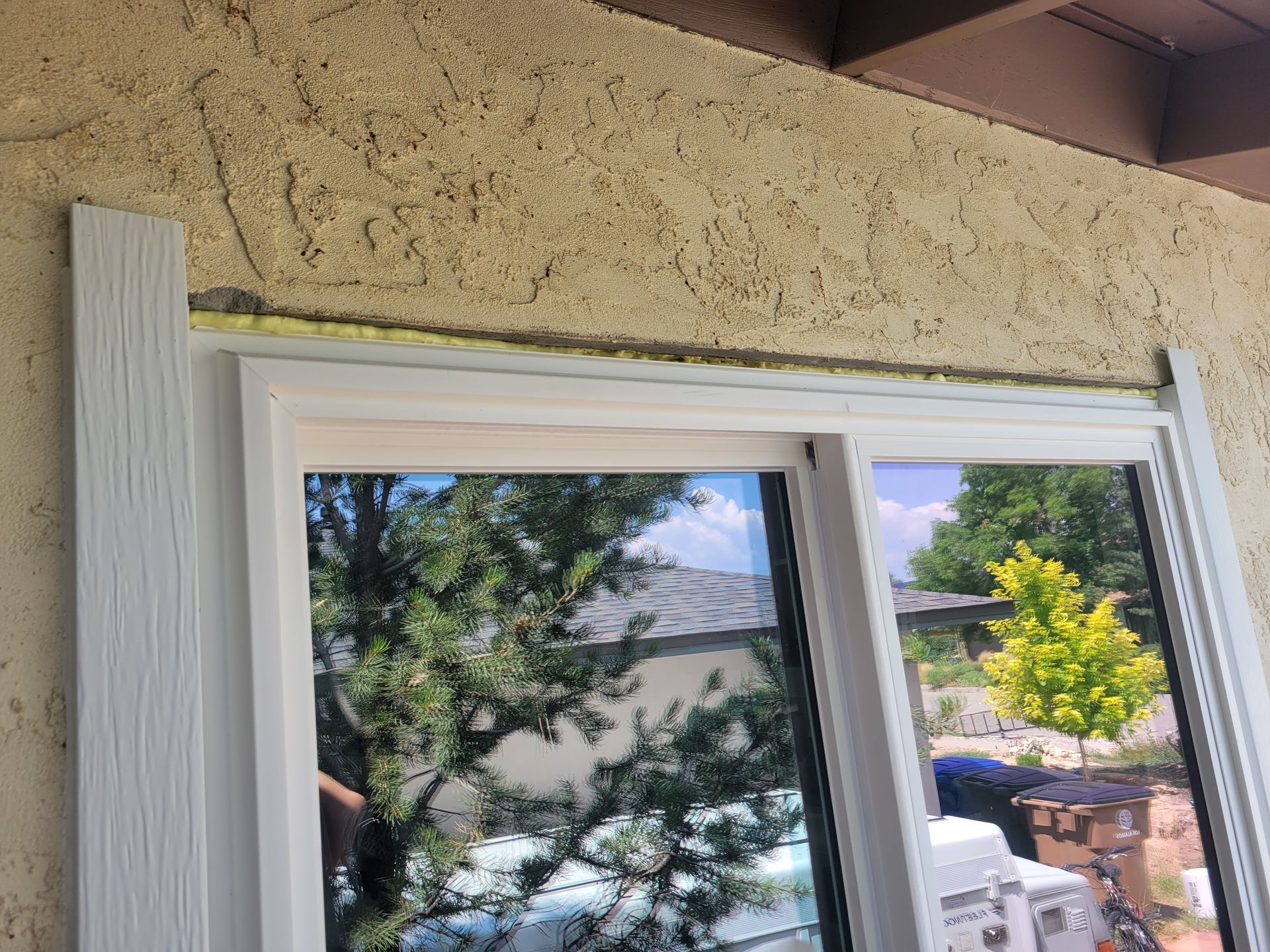 White window installed in stucco wall, with trim on the left. Gap filled with expanding foam.
