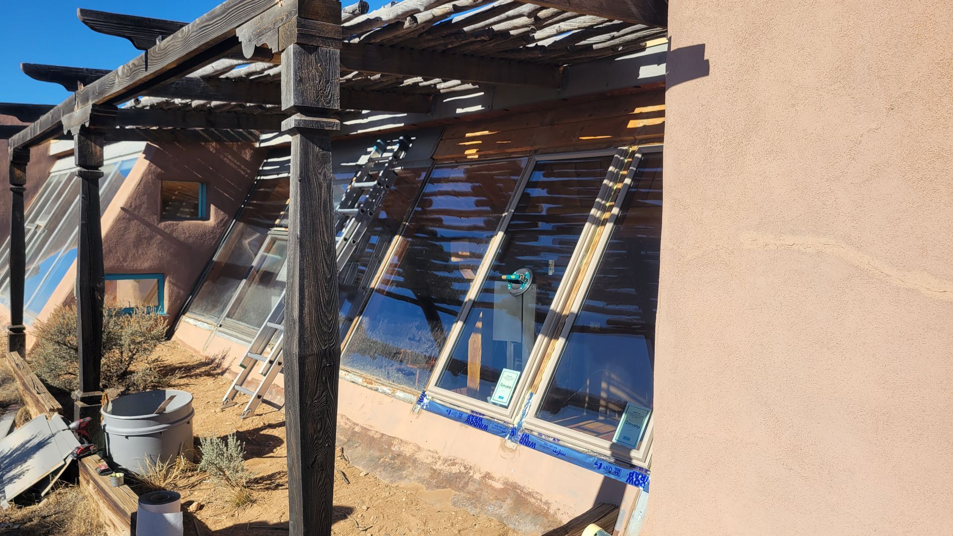 A building with a wooden pergola, angled windows, and tan stucco walls.