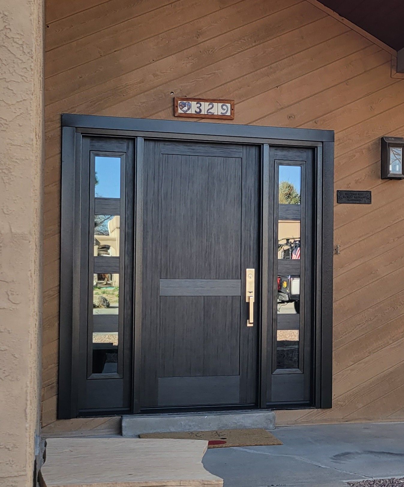 Black front door with sidelights, address plaque on wood siding.