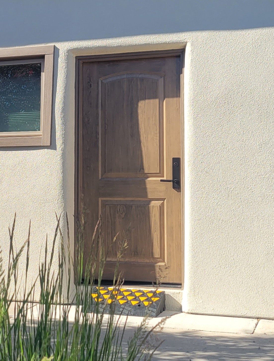 Wooden door in a stucco wall, with a small window and a yellow and black step.