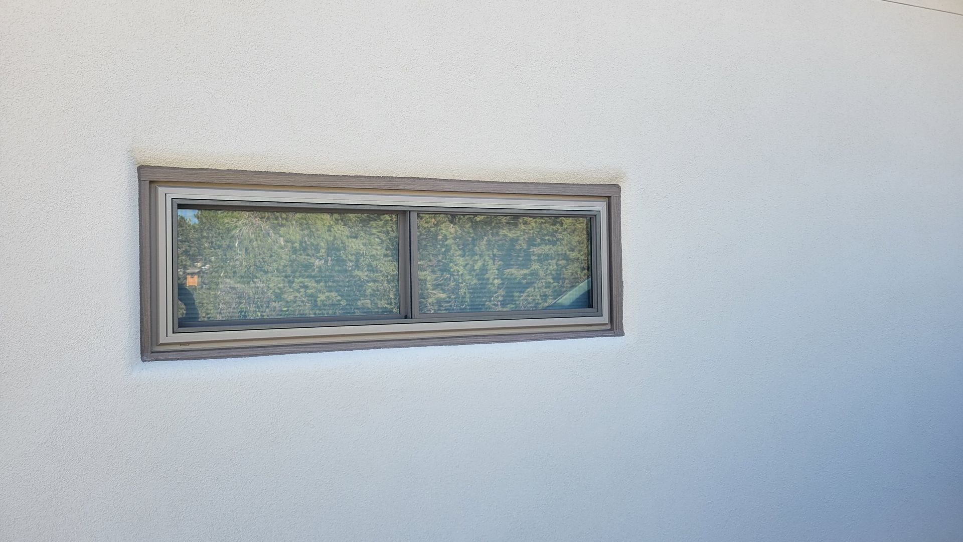 Gray-framed window on a white stucco wall; view through the glass is of greenery.
