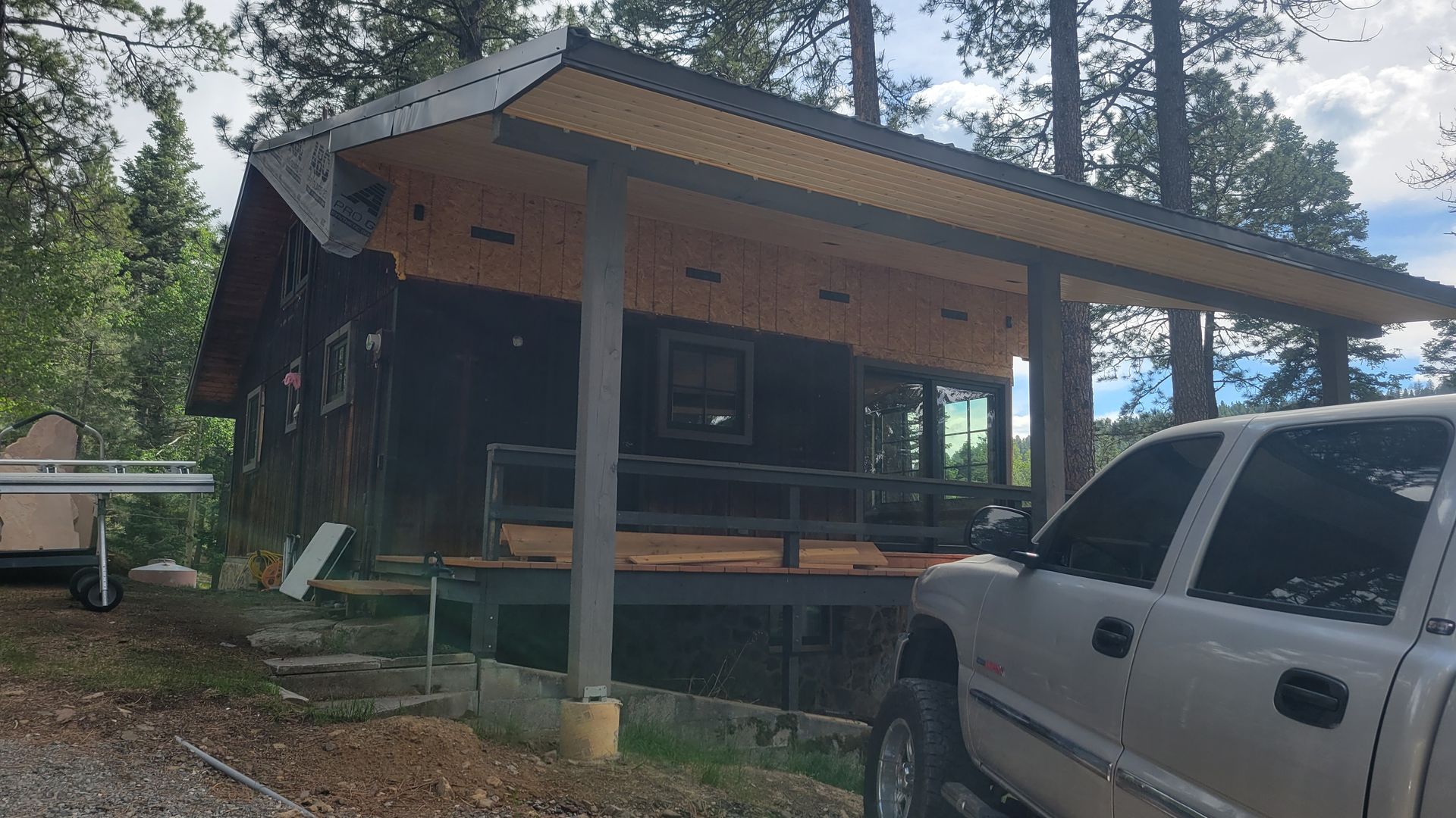Cabin under construction, with a pickup truck parked nearby. The roof is partially completed.