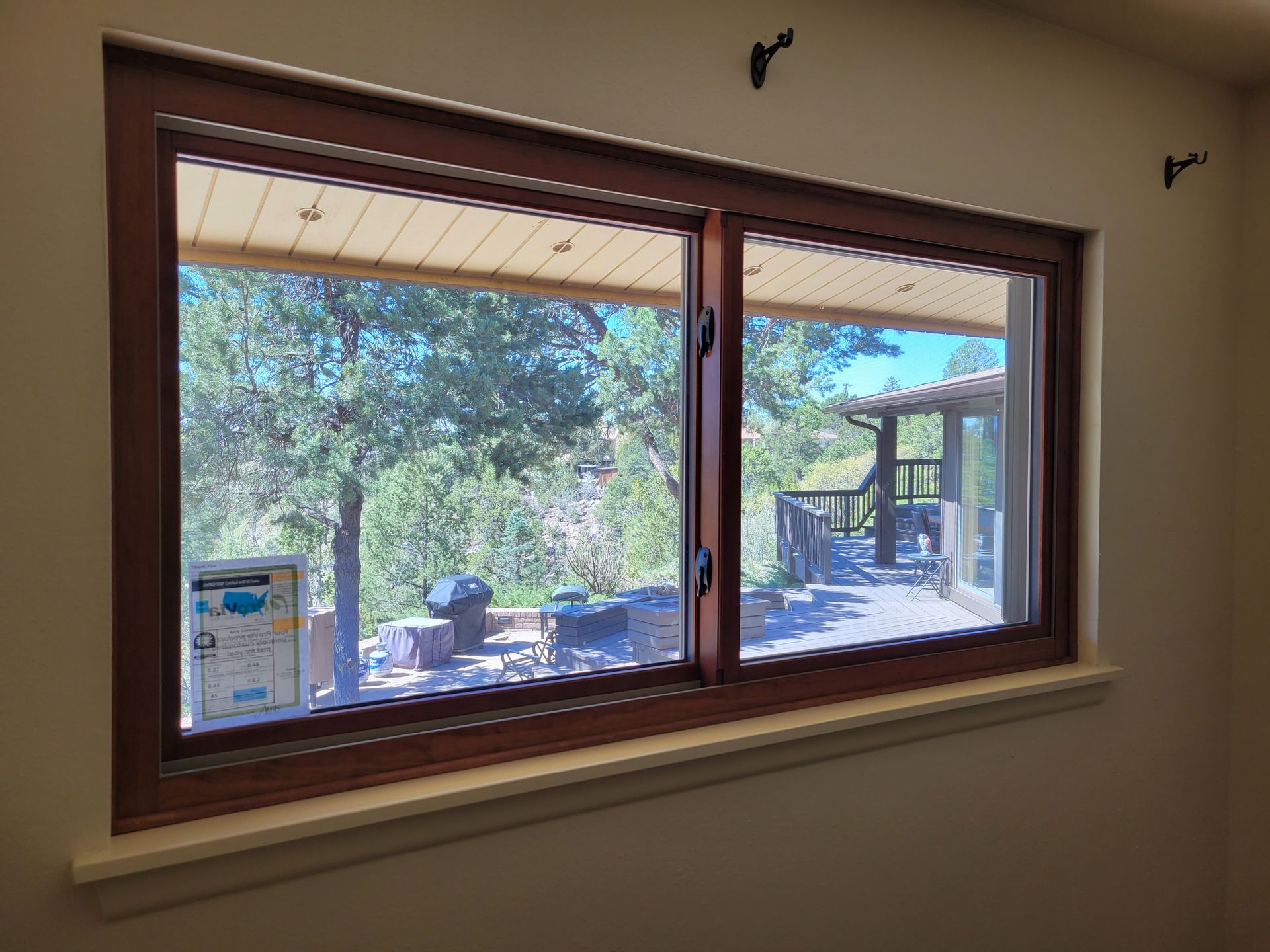 Wooden-framed window overlooking a patio with trees and a deck, seen from inside a room.