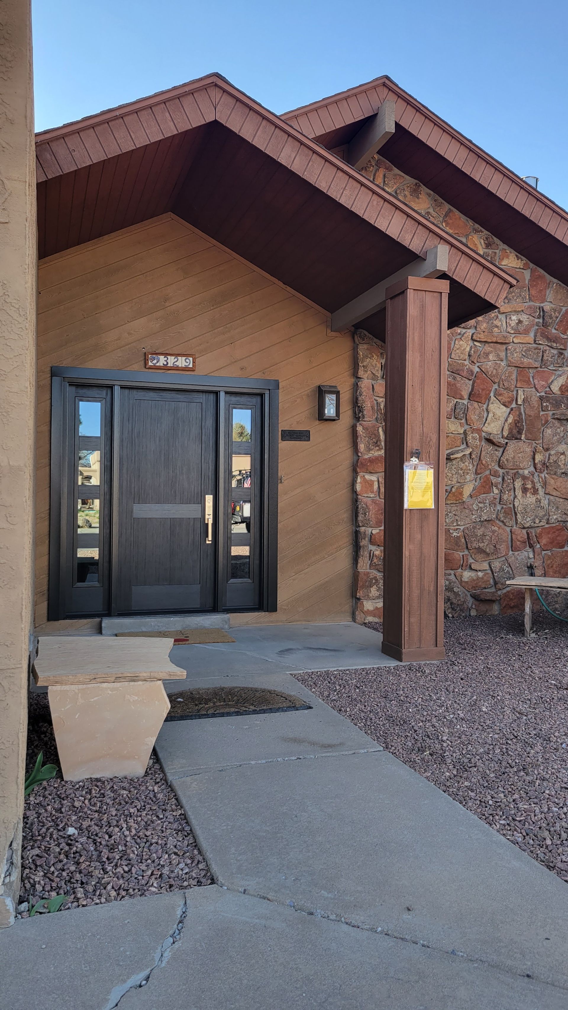 Entrance to a building: dark wood door with sidelights, stone exterior, brown roof, concrete path.