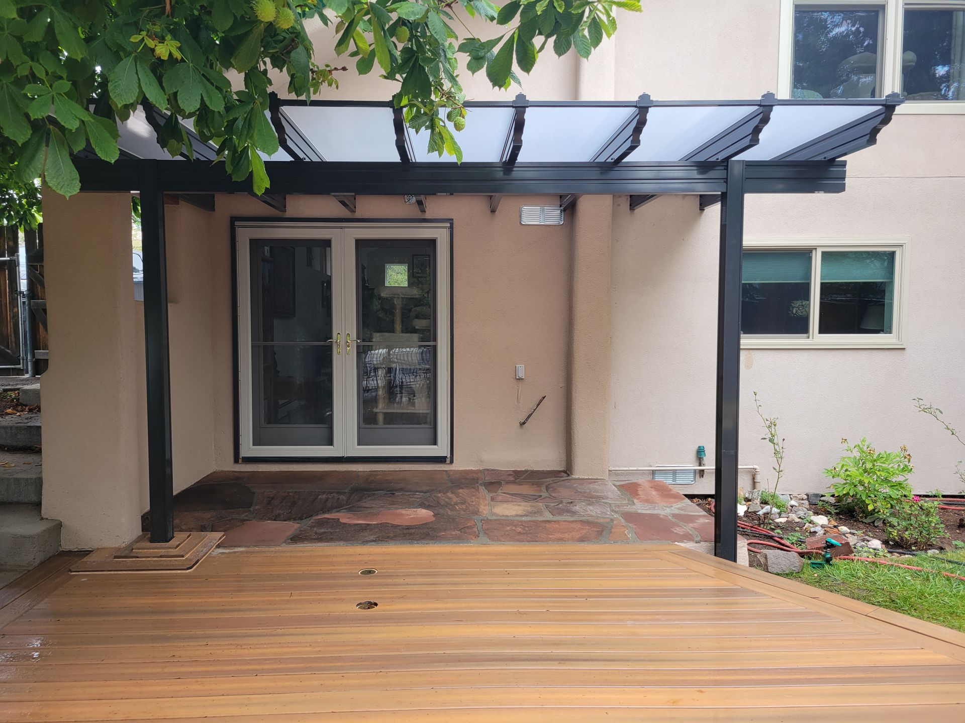 Wooden deck with pergola attached to a beige building with double doors.