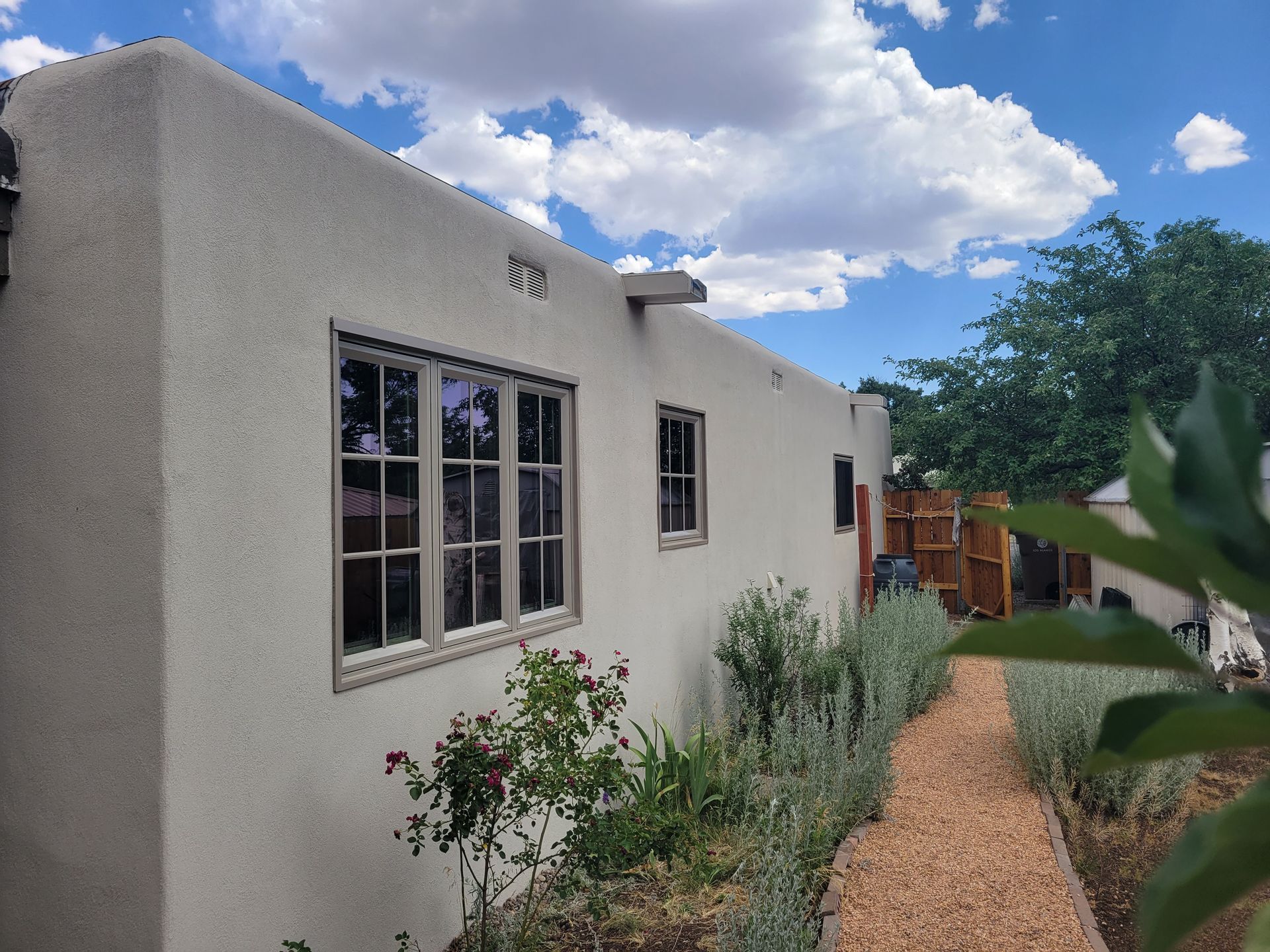 Tan stucco building with windows, a gravel path, and a blue sky with clouds.