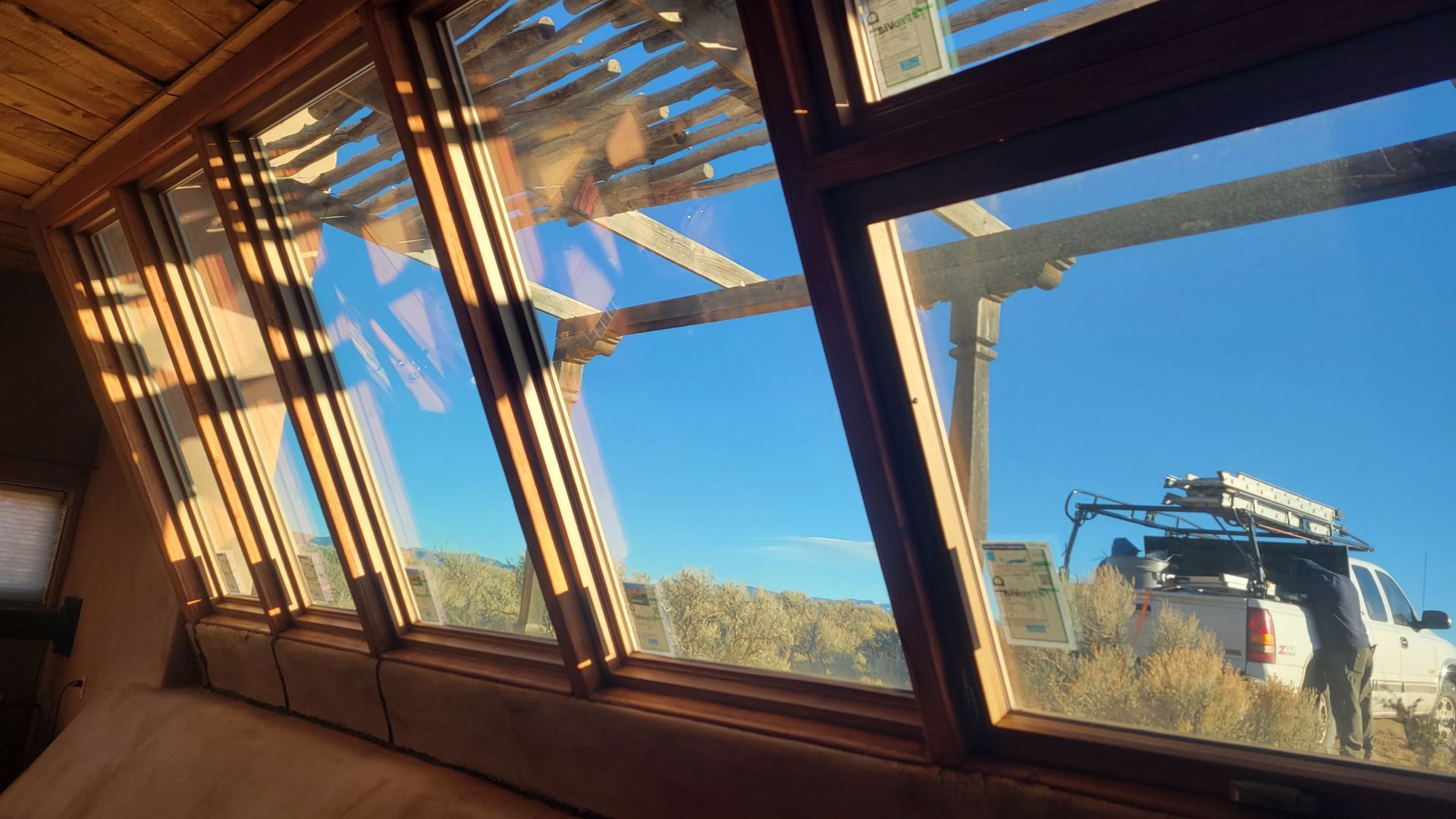 View from inside a building with angled windows, looking out at a truck and blue sky.
