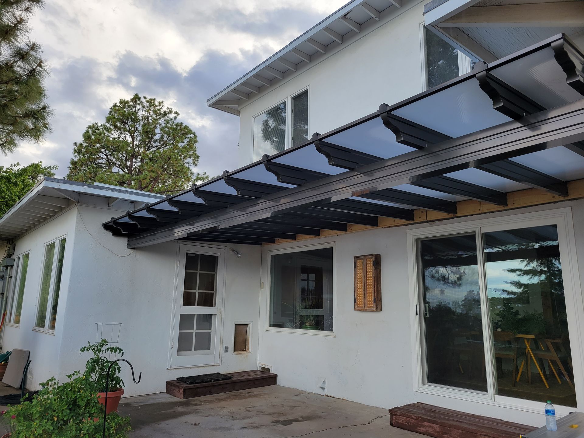 White house exterior with patio, featuring black pergola shade structure and sliding glass doors.