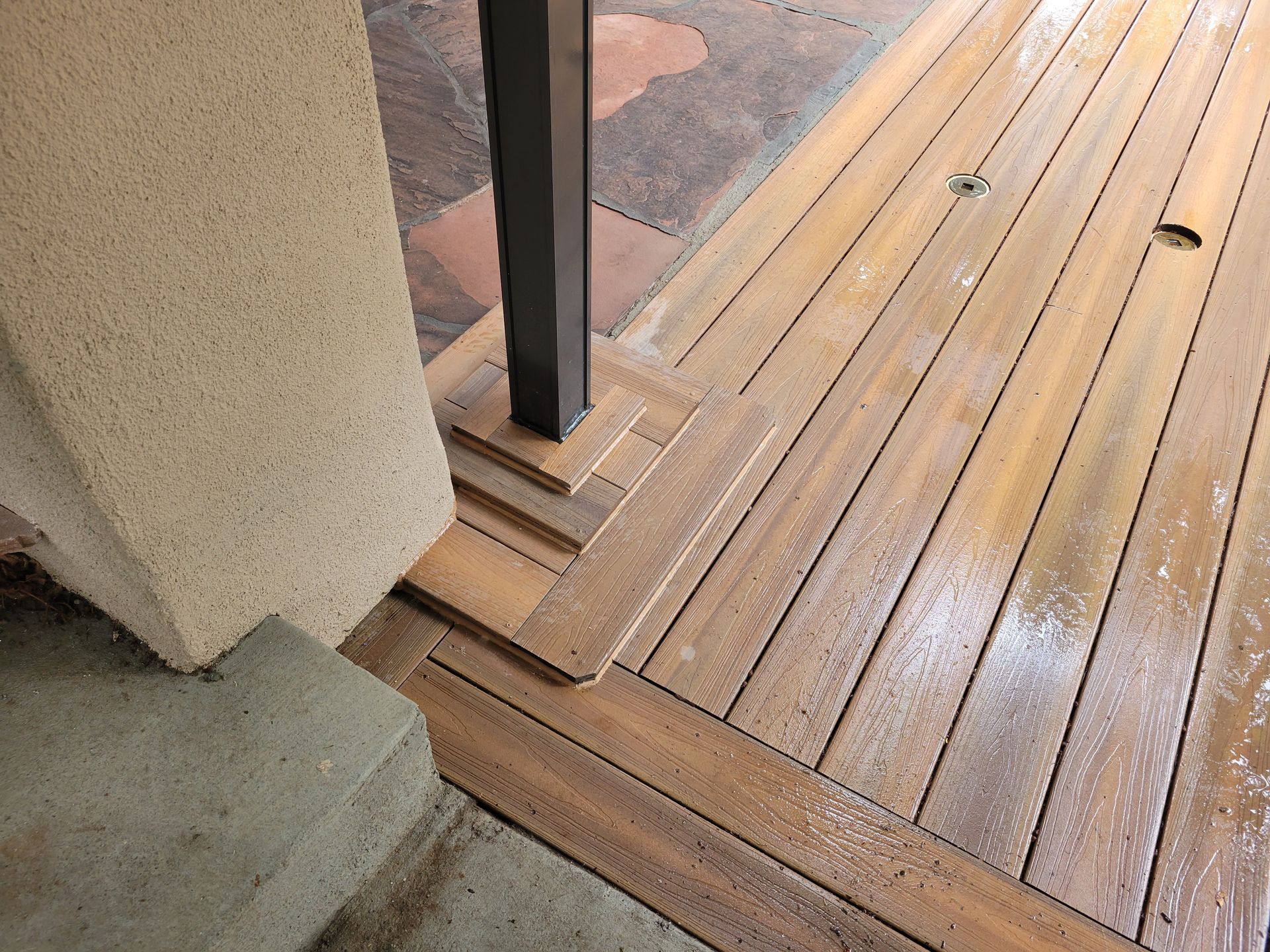 Wooden deck with a step down, next to a concrete wall and post.