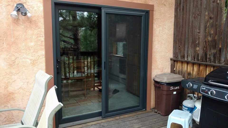 Sliding glass door with screen open, revealing a patio with seating, grill, and trash can.