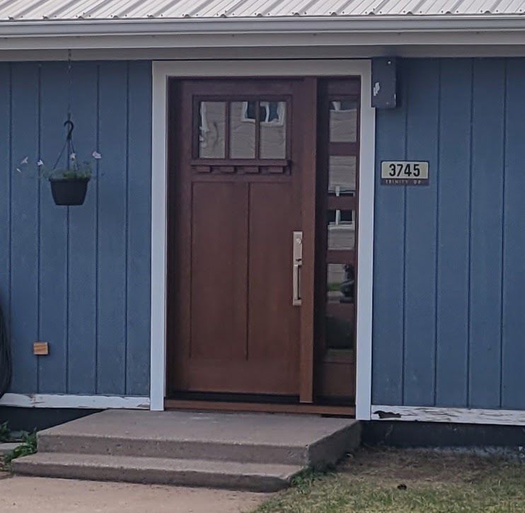 Brown front door with sidelight and transom, light blue siding, white trim, address plaque.