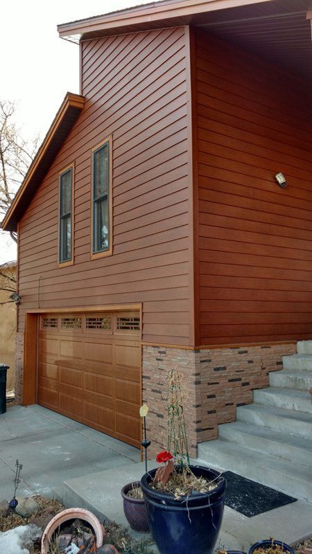 Brown house with garage, windows, and steps, featuring brown siding and stone base.