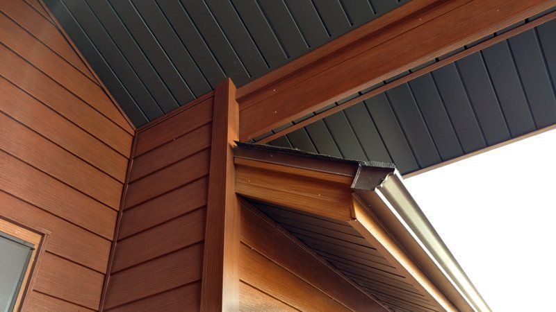 Brown siding and wooden trim on a building's exterior, with a dark ceiling and a gutter.