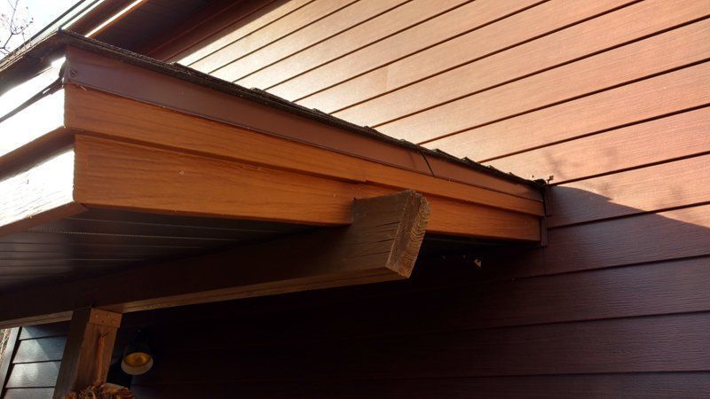 Wooden eaves over a dark brown wall with horizontal siding, supported by a wooden bracket.