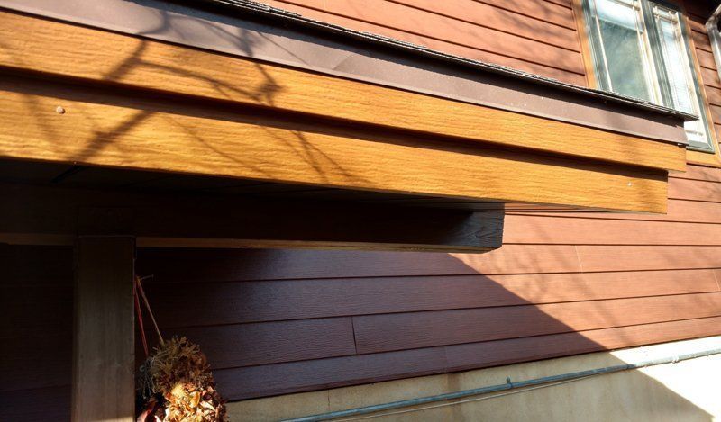 Wooden awning over a brown-sided building, casting shadows in the sunlight.