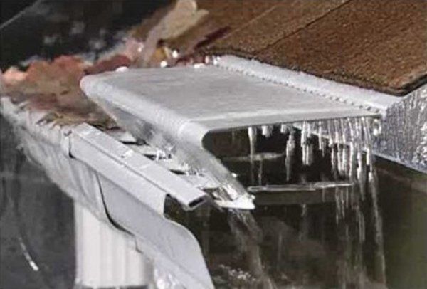 Frozen gutter with ice, overflowing water, and gutter guard installed.
