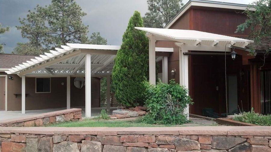 House exterior with white pergolas, brown siding, and stone wall in front.