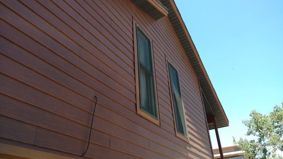 Brown wood-sided building with two tall windows and blue sky above.