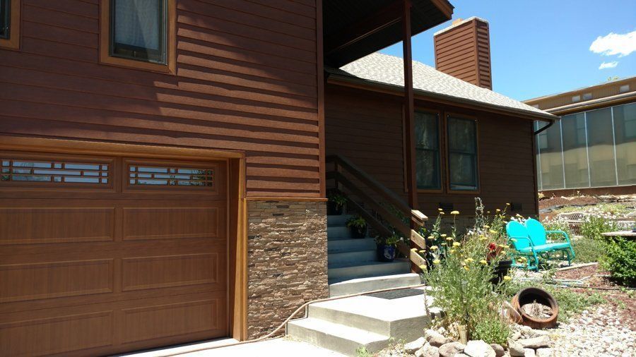 Brown house with garage, entrance steps, and blue bench outside.