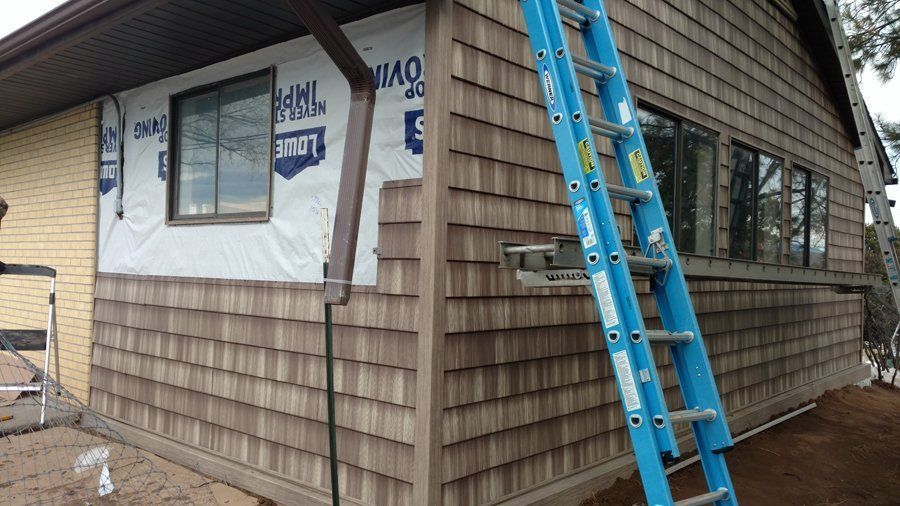 House exterior under renovation with cedar shingles and blue ladder.