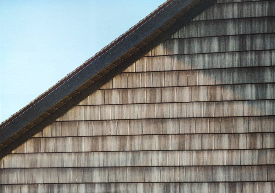 Wood shingle siding on a building's roof corner, with a dark wooden beam and clear sky background.