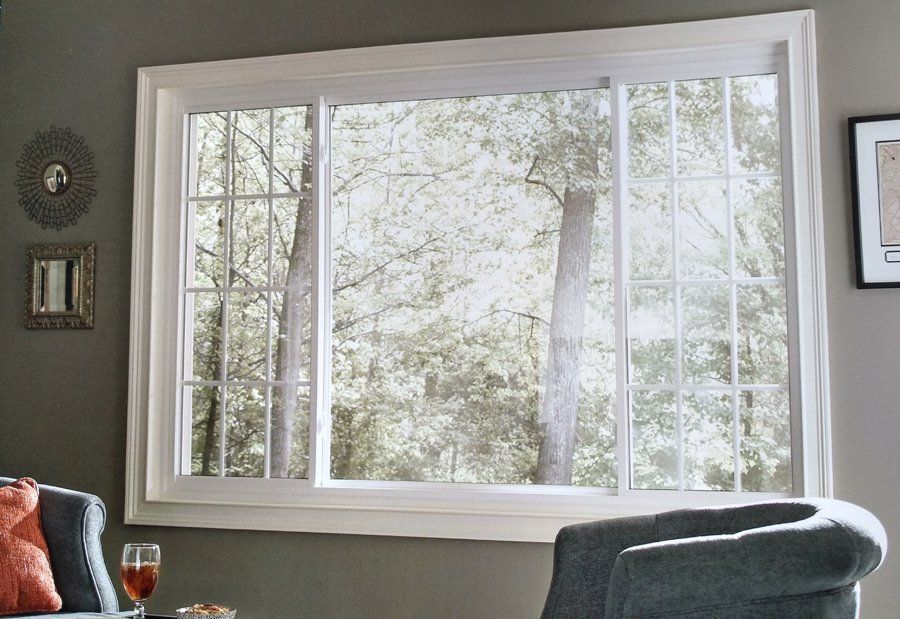Large white-framed window looking out onto trees; a gray armchair and wall decorations are also visible.