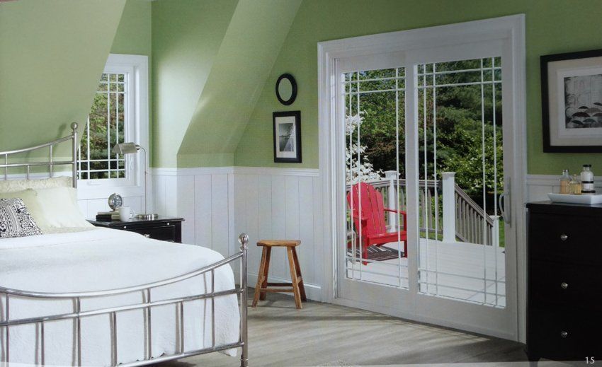 Bedroom with green walls, white wainscoting, a bed, a doorway to a balcony with a red chair.
