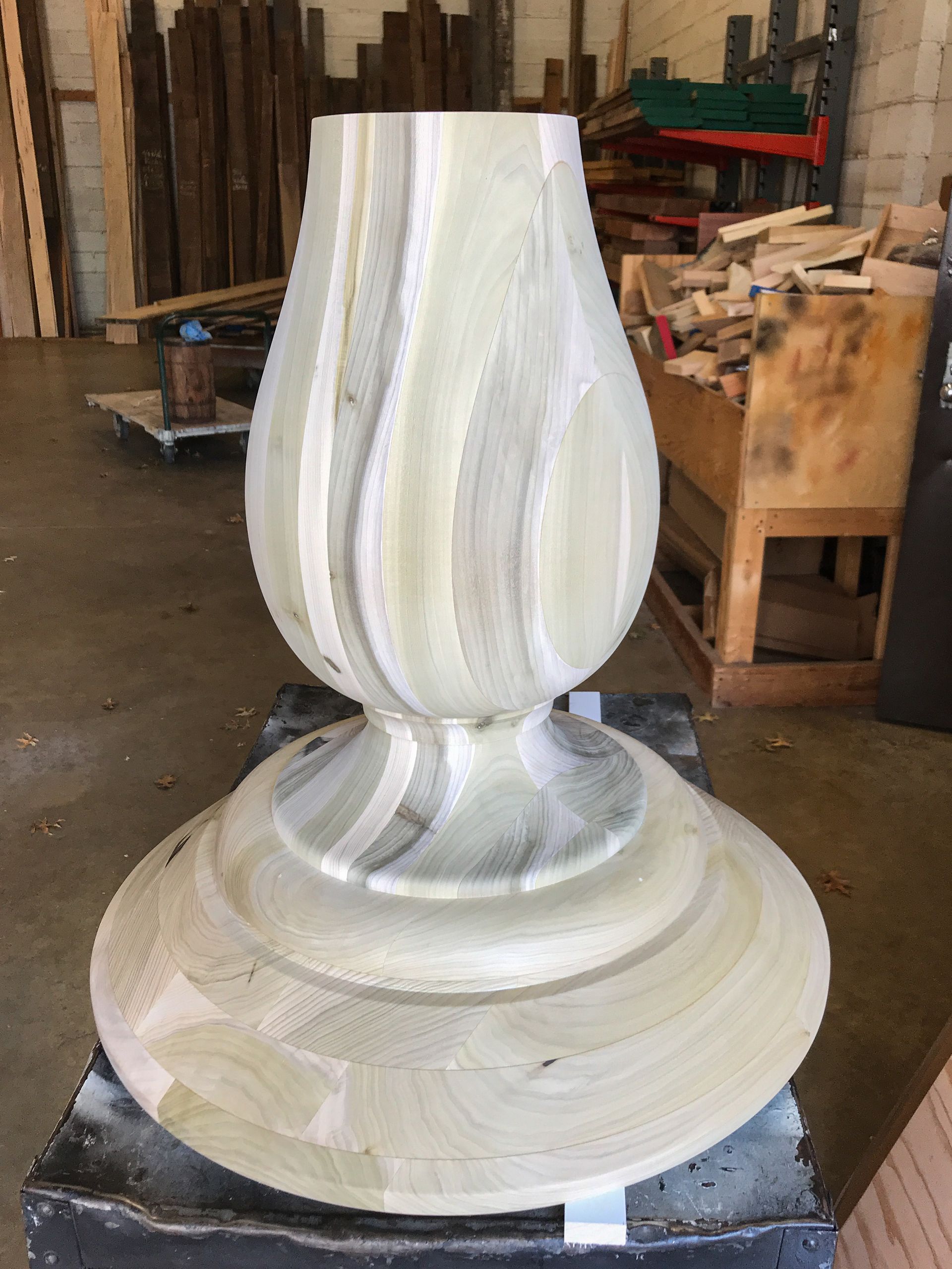 Wooden table base with bulbous center and circular foot, in a workshop.