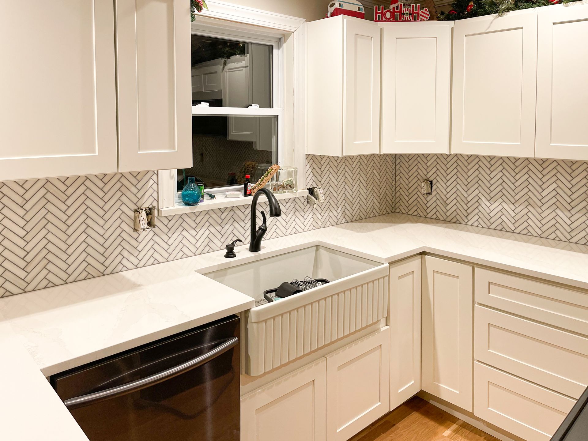 White kitchen with herringbone backsplash, farmhouse sink, and black faucet.