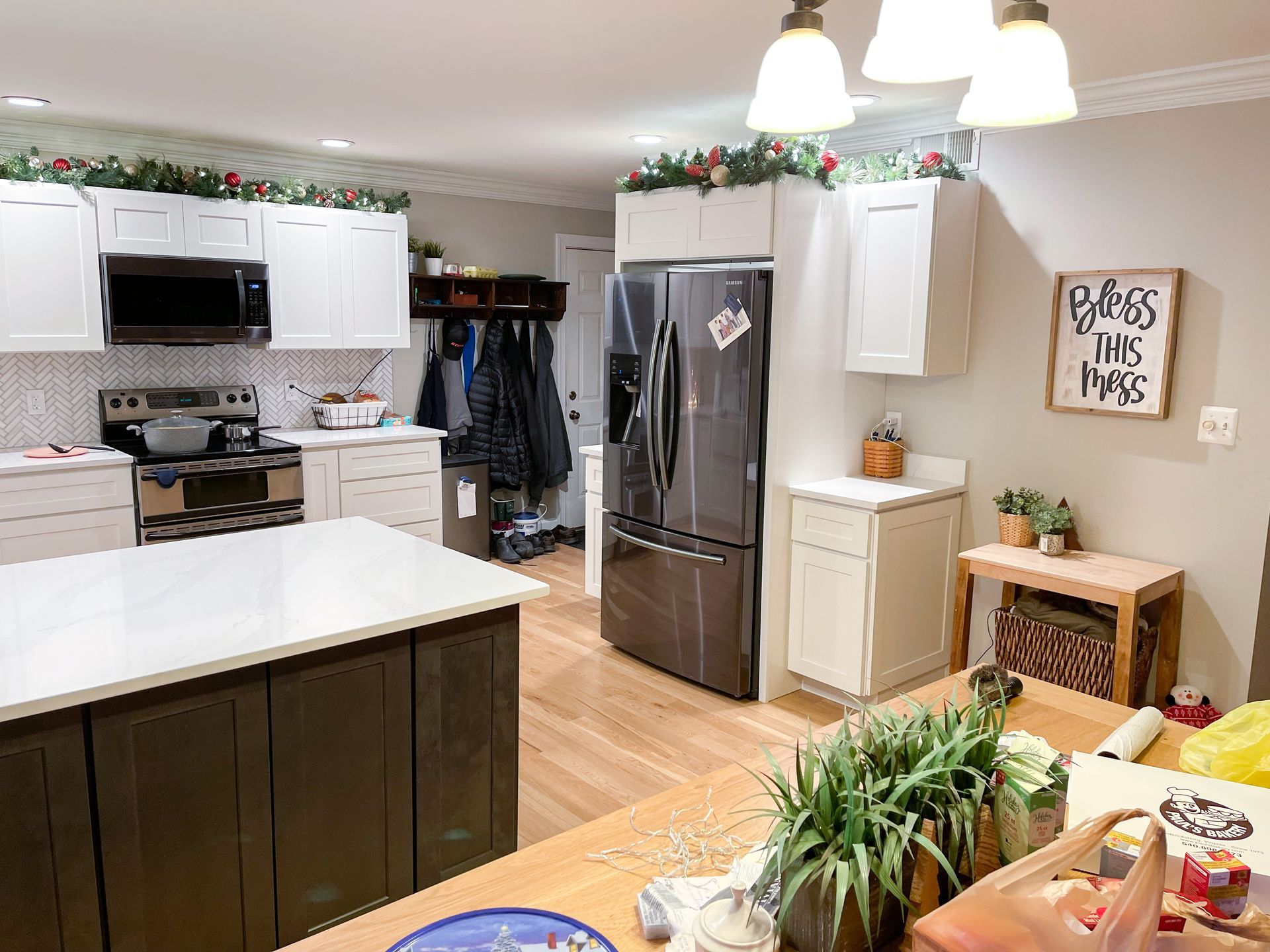 Kitchen with white cabinets, dark island, stainless steel appliances, and wood floors.