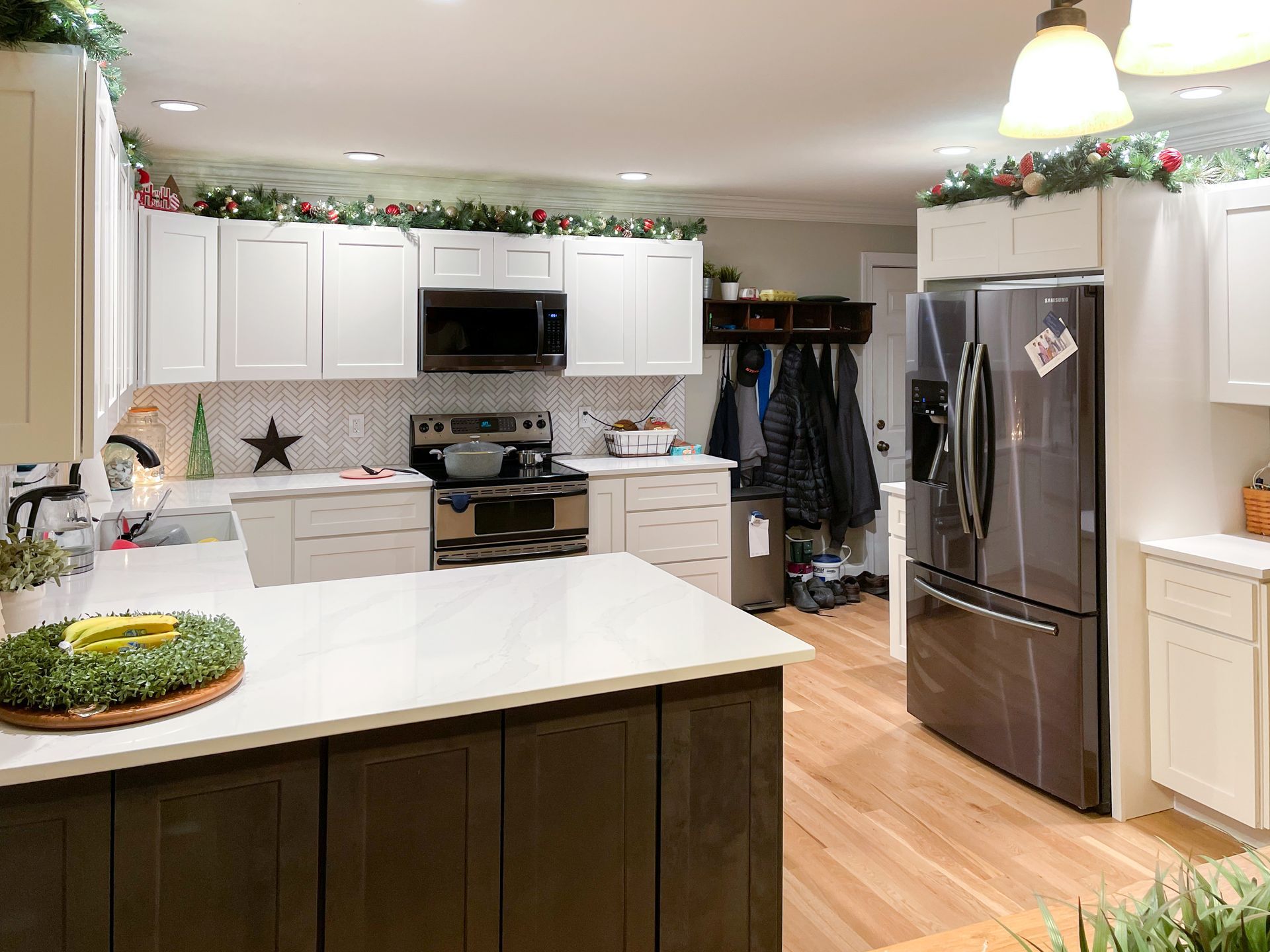 Kitchen with white cabinets, dark island, stainless steel appliances, and festive greenery.