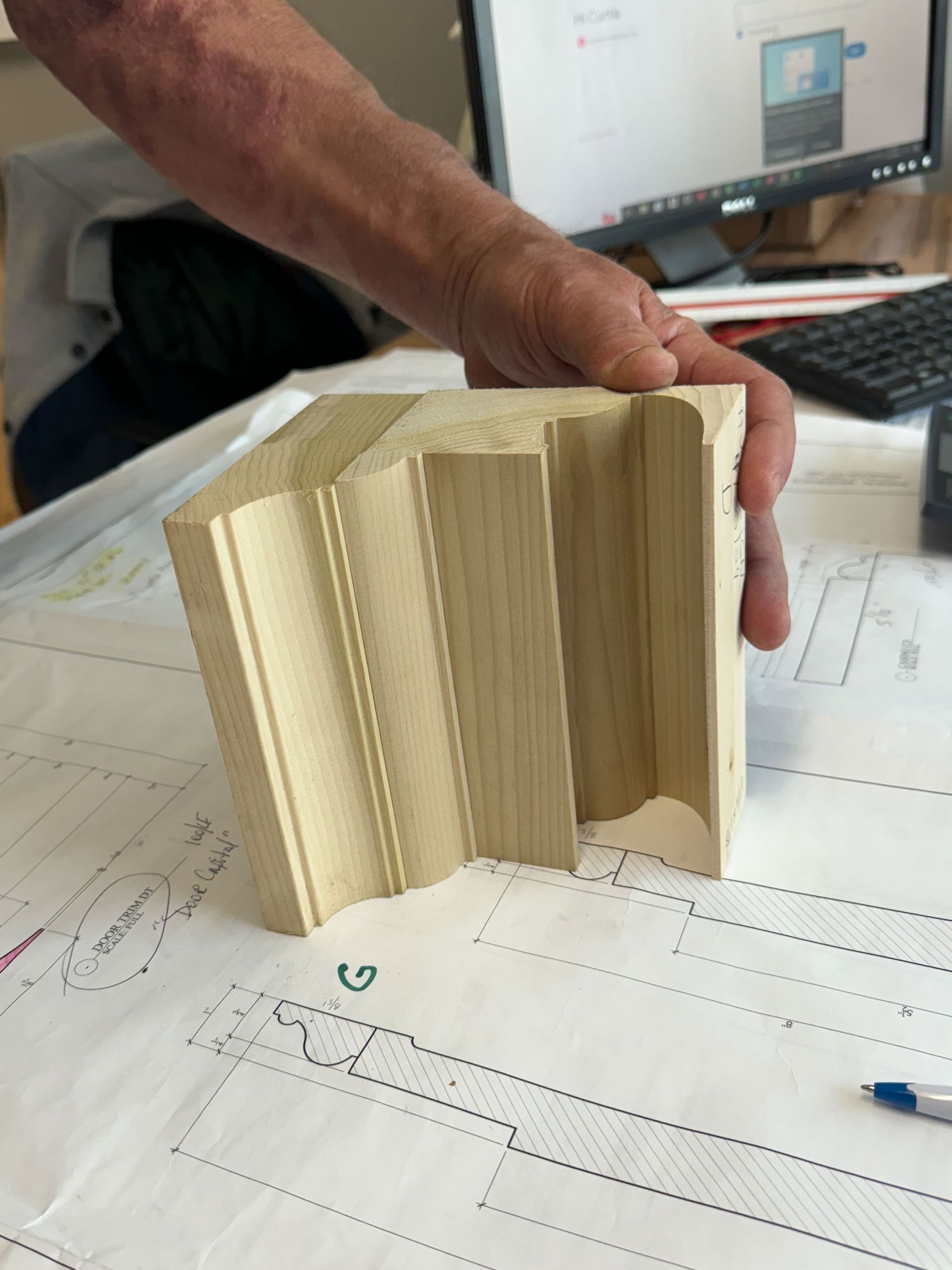 A person holds a carved wooden architectural detail over a blueprint.