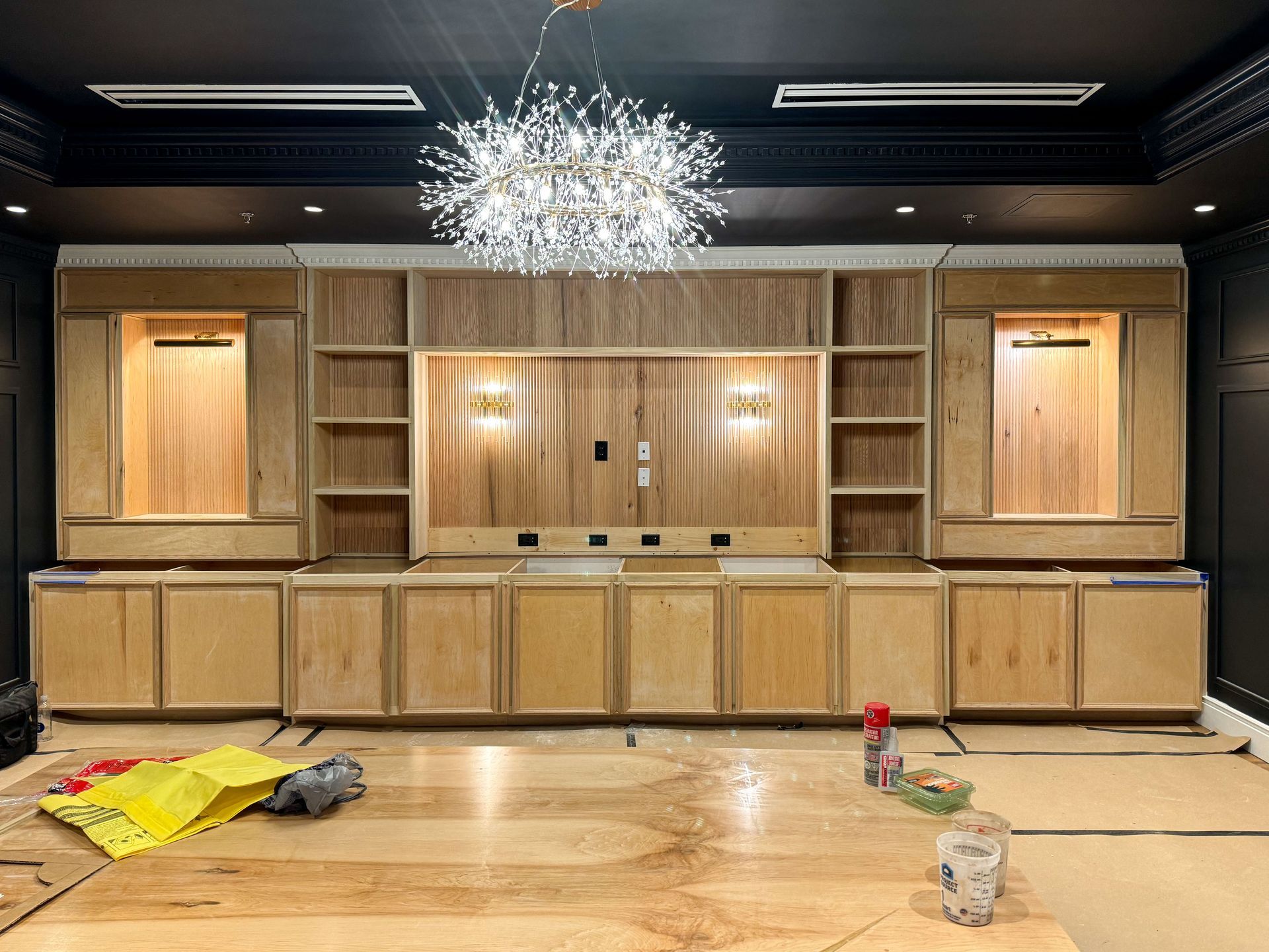 Wooden built-in media center with cabinets, shelves, and a decorative light fixture, under construction.