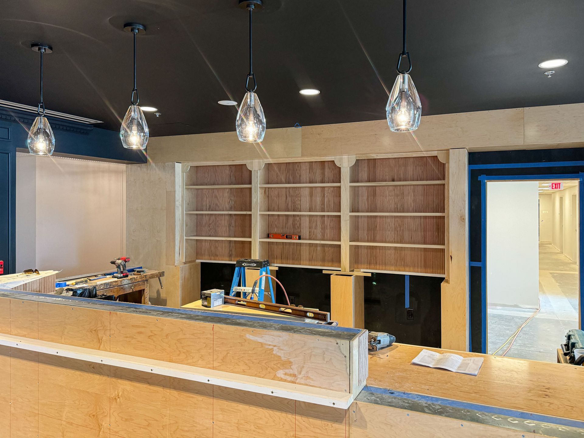 Interior under construction with overhead lights, exposed shelving, and a partially built counter.