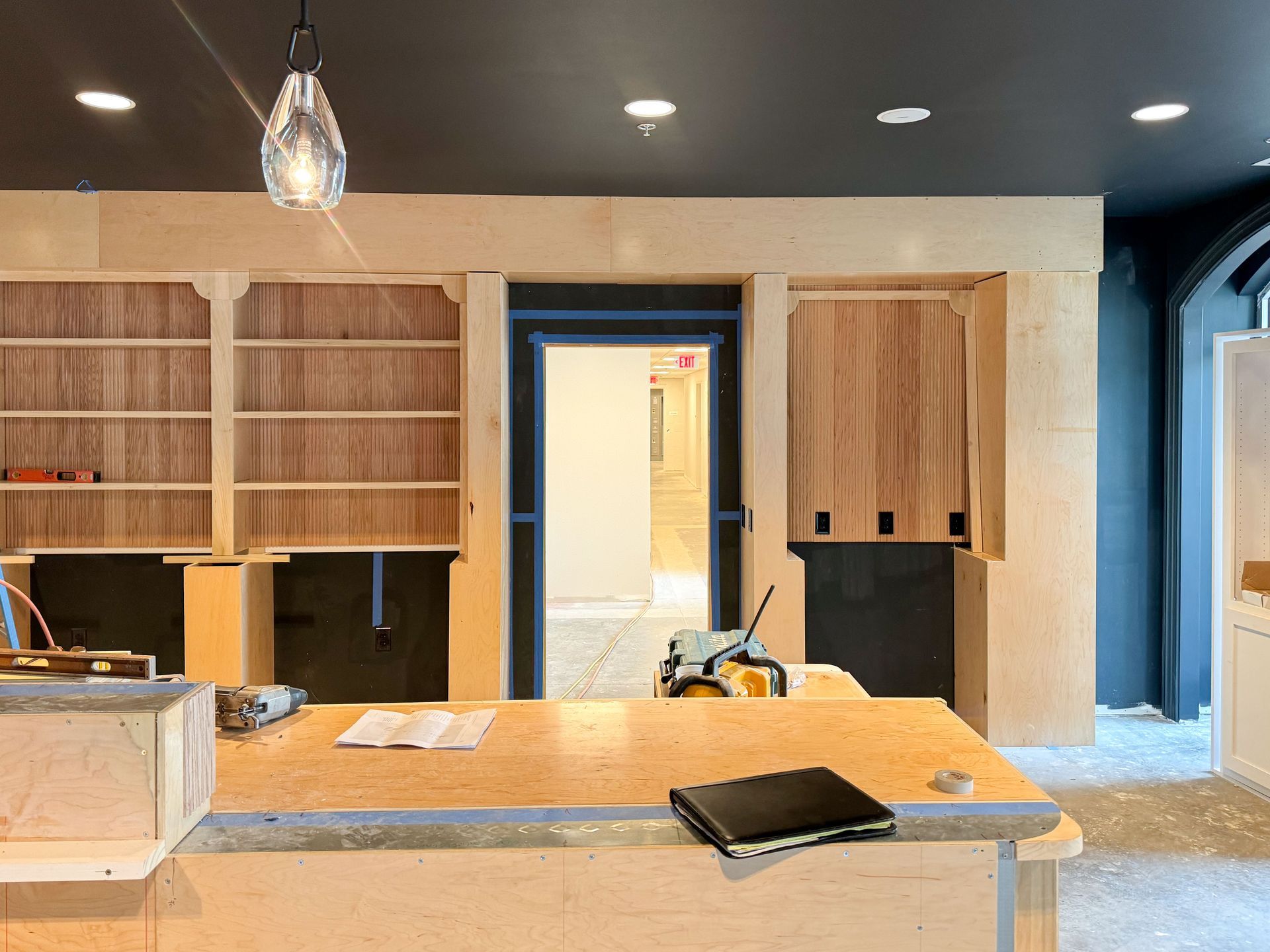 Interior construction site with wooden shelving, a counter, and open doorway to another room.