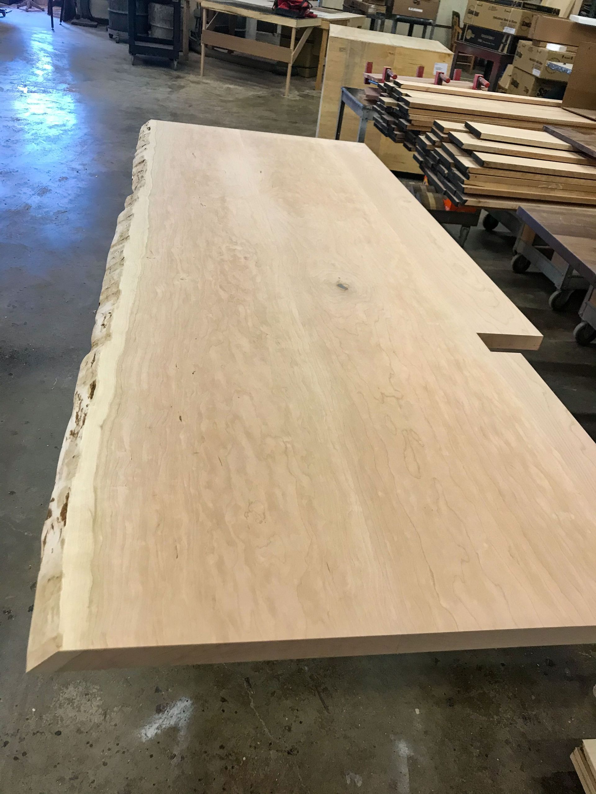 Large, unfinished wooden slab with live edge in a workshop.