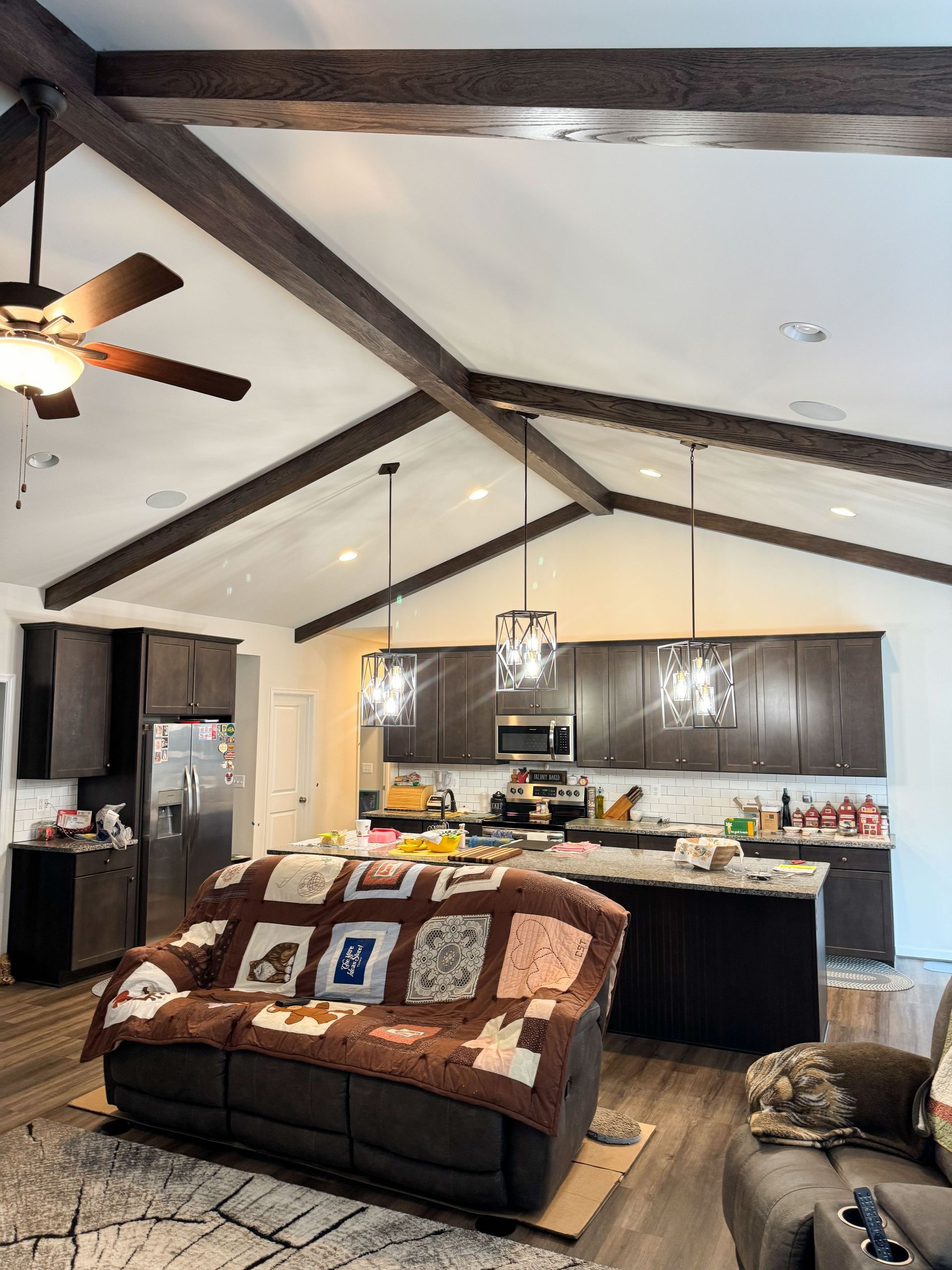 Living room with brown cabinets, dark ceiling beams, and a brown sofa covered with a quilt.