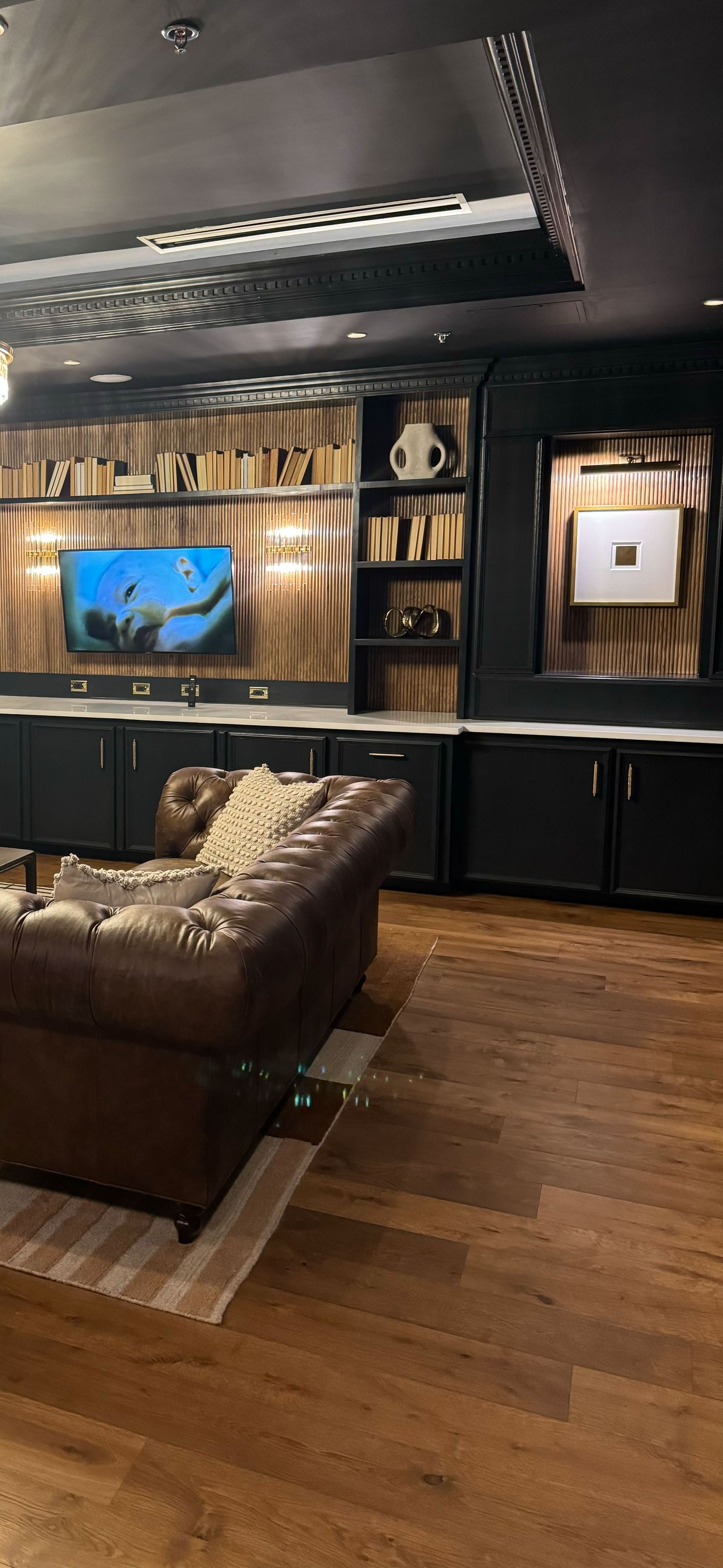 A room with a brown leather couch, wooden floors, and a built-in entertainment center with a TV and shelves.