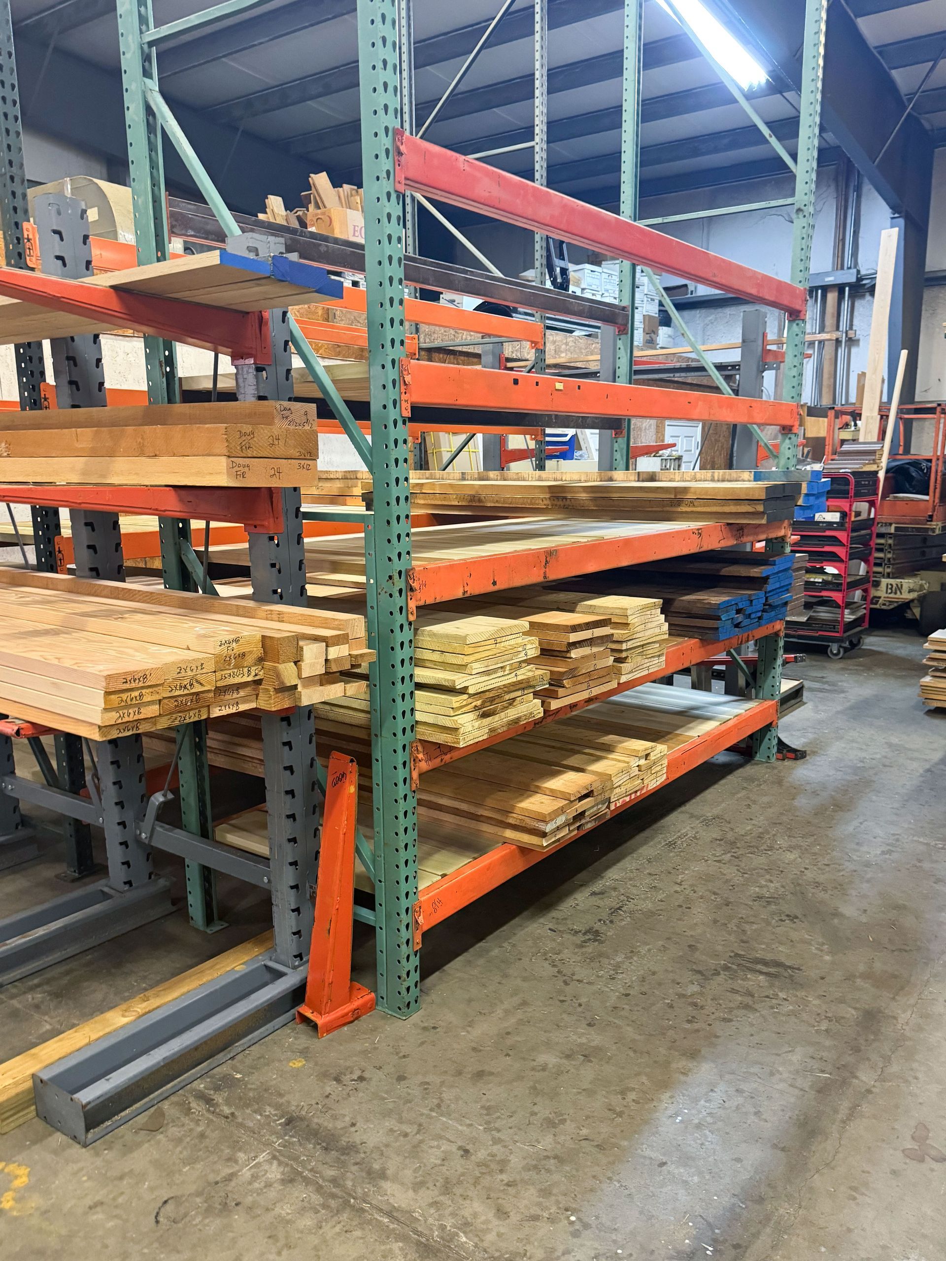 Shelves filled with various lumber inside a warehouse, with a concrete floor.