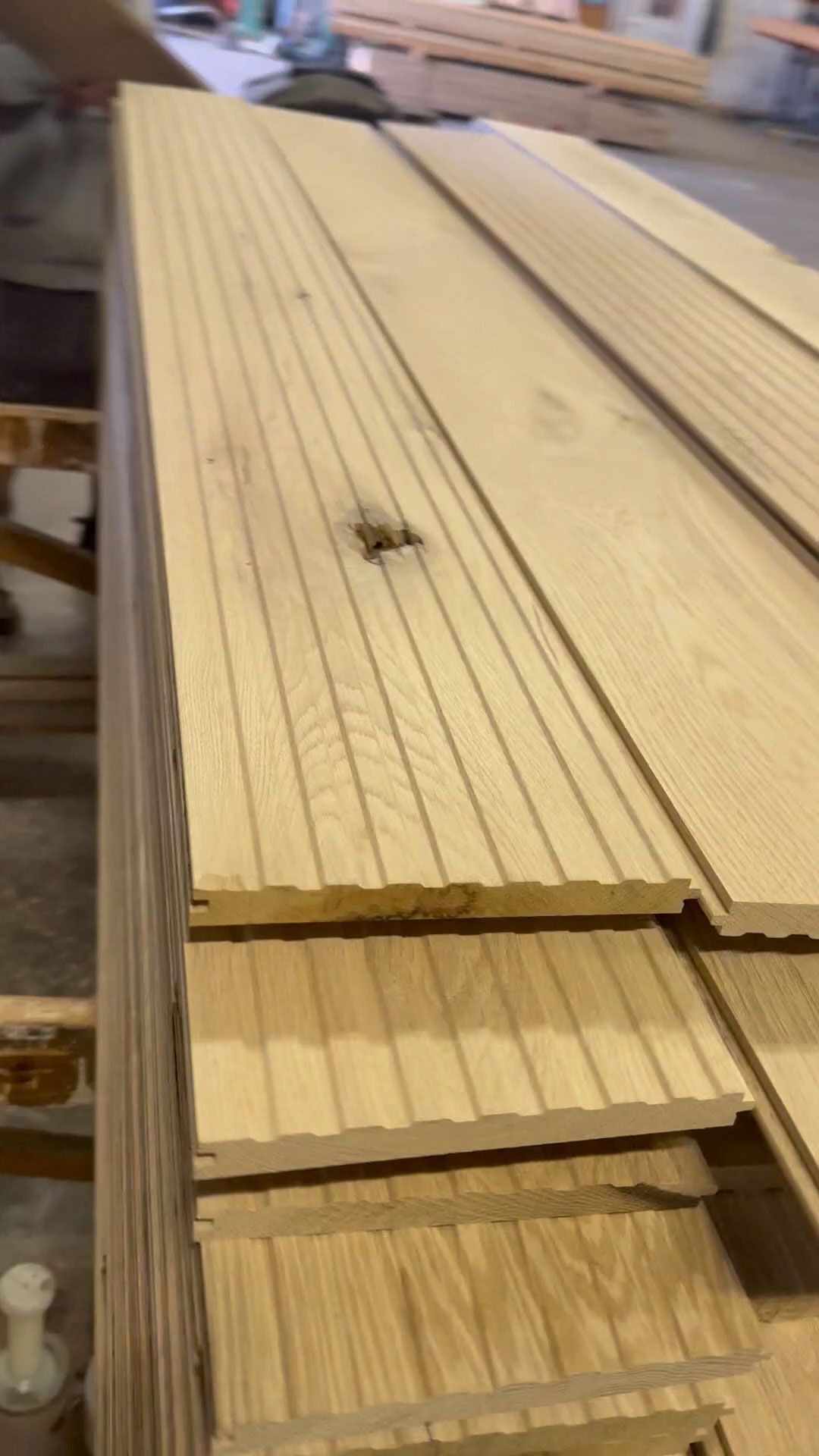 Stack of light-colored wooden boards with grooved surfaces, possibly for flooring or paneling.