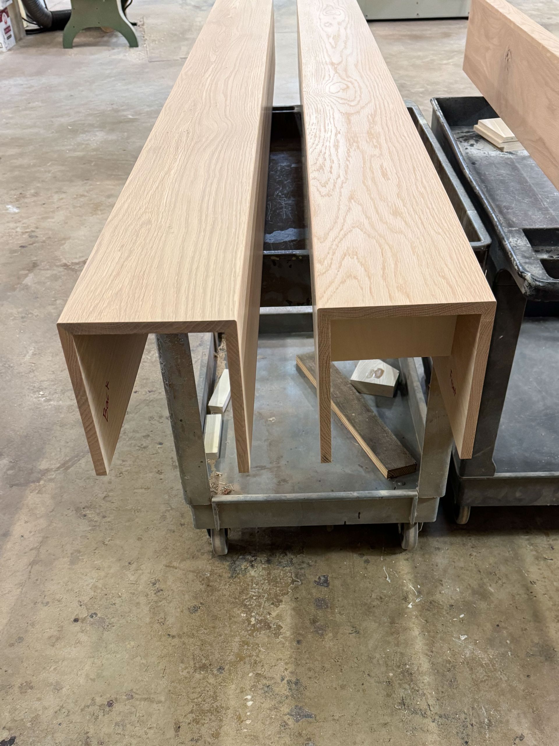 Two unfinished wooden structures sit on a metal wheeled cart in a workshop setting.