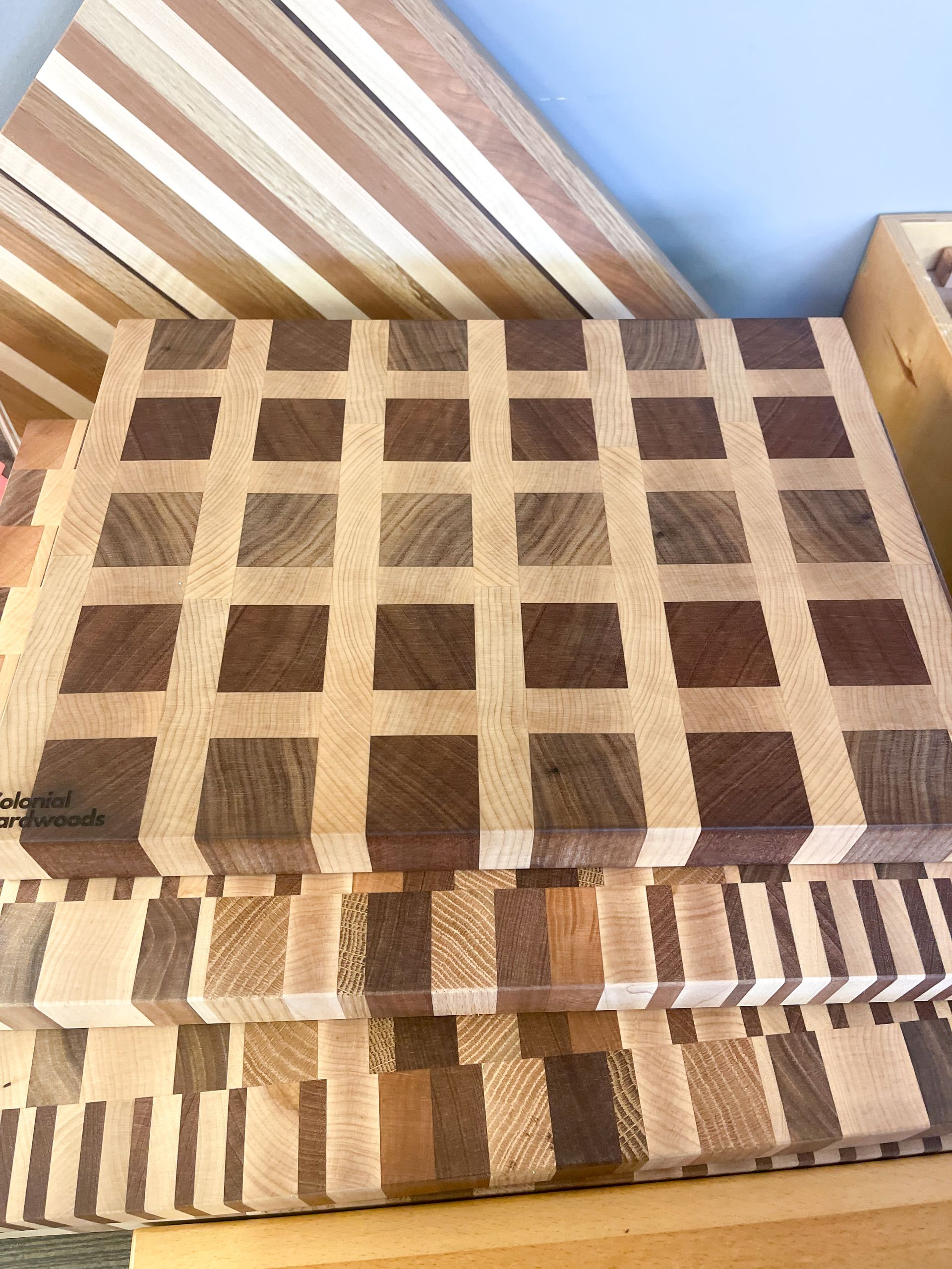 Wooden cutting boards stacked, showing checkered and striped patterns, varying shades of brown.