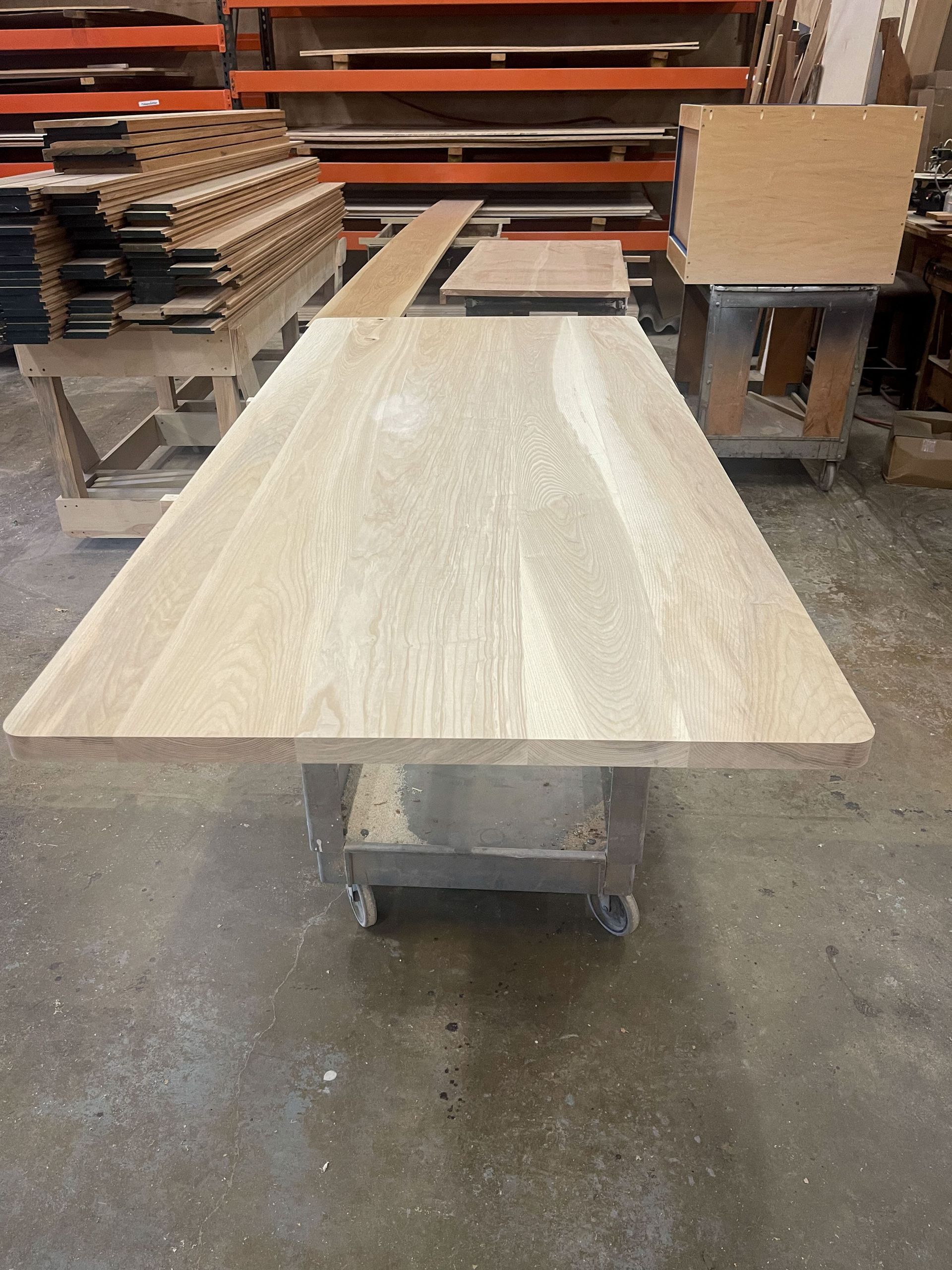 Wooden table top, light brown, on a rolling workbench in a workshop.