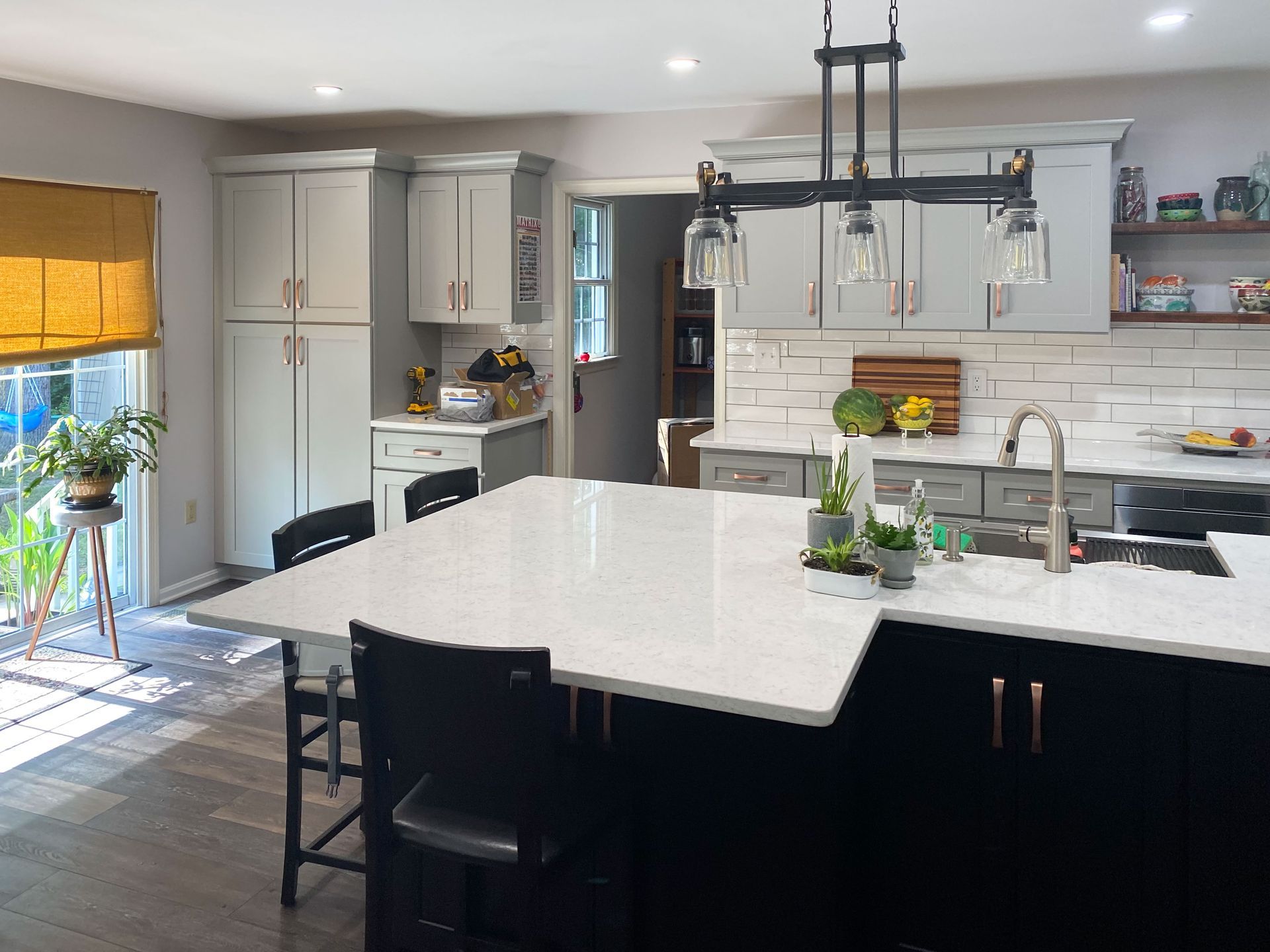 Modern kitchen with gray cabinets, black island with white countertop, and yellow shade over a window.